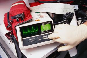 Hand in rubber glove pressing button on defibrillation monitor