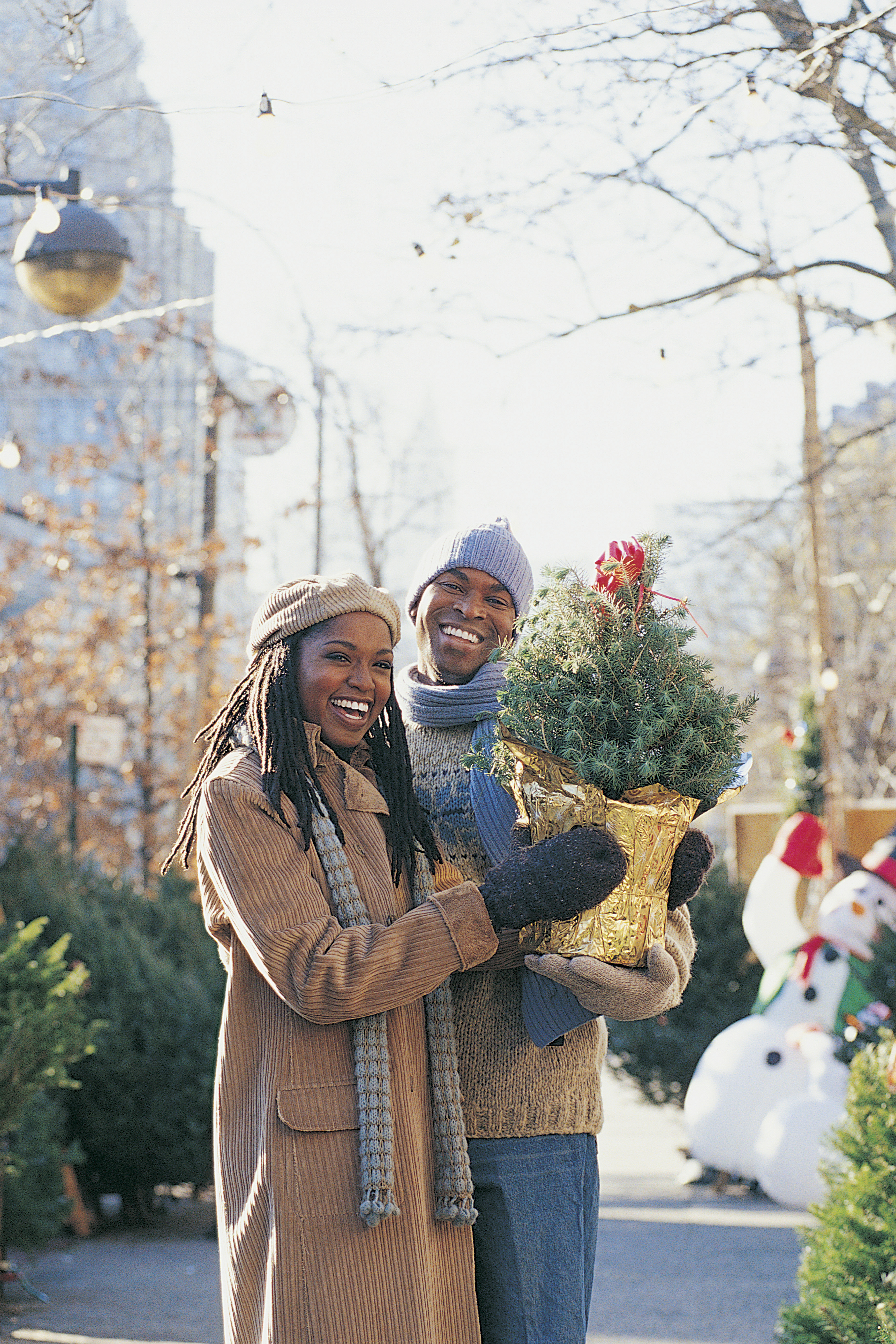 Young Couple Standing in a City Street Holding a Small Christmas Tree