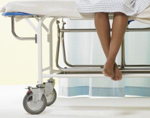 Female patient sitting on gurney in hospital gown, low section
